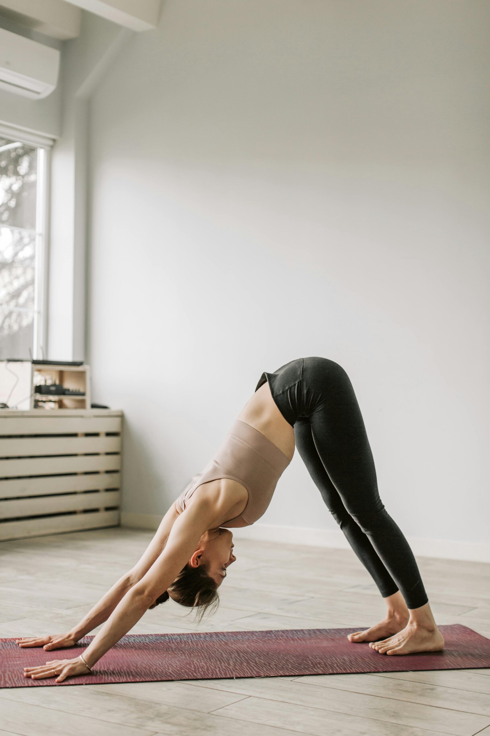Adult woman in a downward facing dog yoga pose on a mat indoors during daytime.