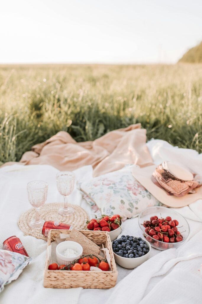 A serene summer picnic setup with fresh fruits and a blanket in a lush green field.